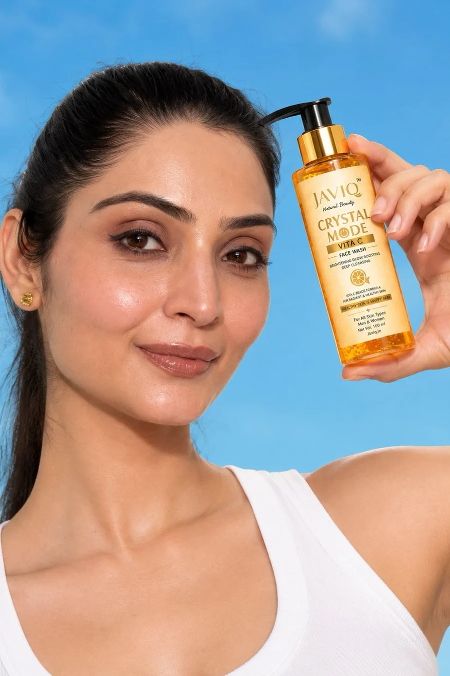 Woman holding JAVIQ Crystal Mode Vita C face wash against a blue sky